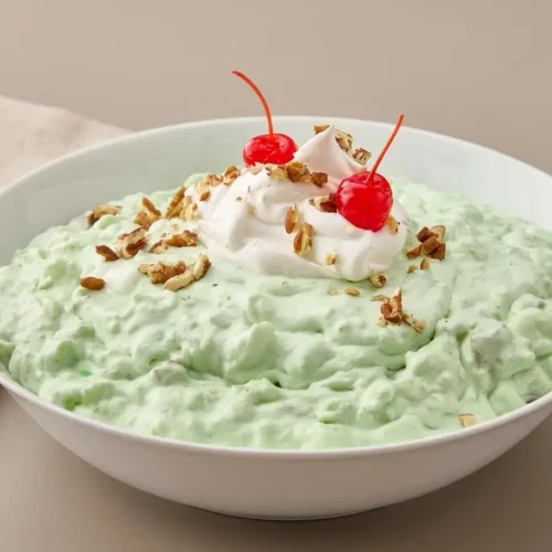 Chilled watergate salad recipe served in a glass bowl with creamy pale green fluff and chopped pecans.