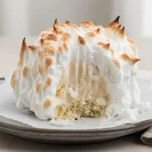 Individual baked alaska recipe portion with toasted golden meringue peaks over pound cake and vanilla ice cream.