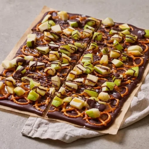 Shards of caramel apple bark with glossy dark chocolate, diced green apple, pretzels, and rich caramel drizzle.