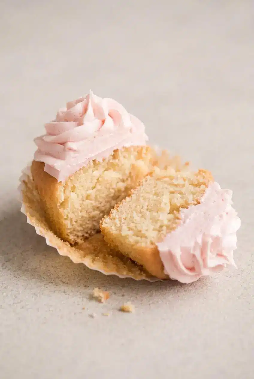 Split pink champagne cupcake showing a tender, aerated interior crumb and smooth piped frosting.