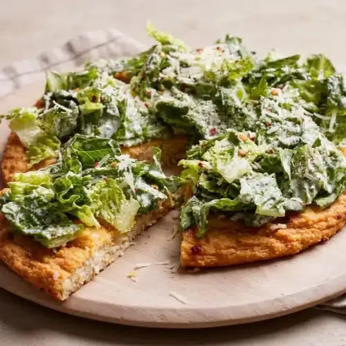 Chicken crust caesar salad pizza with a crispy golden Parmesan edge topped with creamy dressed romaine lettuce.