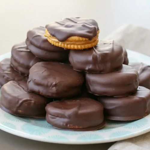 Chocolate peanut butter ritz cracker cookies stacked on a plate with a smooth, firm chocolate shell.