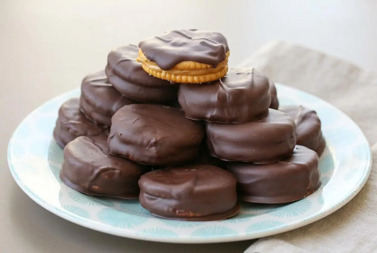 Chocolate peanut butter ritz cracker cookies stacked on a plate with a smooth, firm chocolate shell.