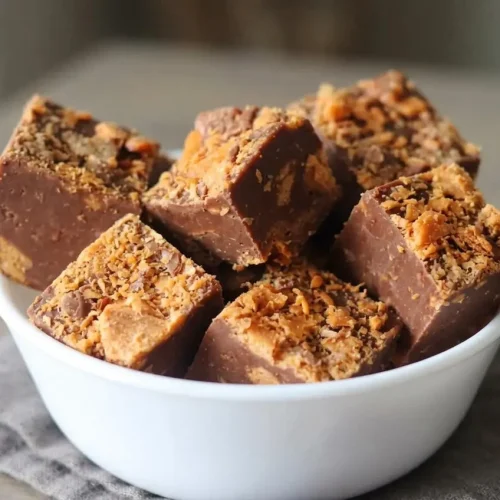 Creamy chocolate and peanut butter butterfinger fudge squares topped with crispy chopped candy bar pieces