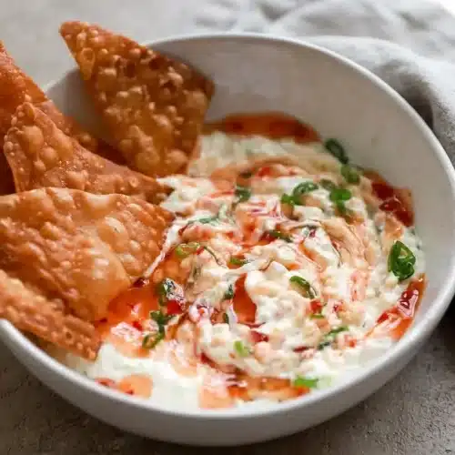 Creamy crab rangoon dip topped with glossy sweet chili sauce and scallions alongside crispy fried wonton chips.