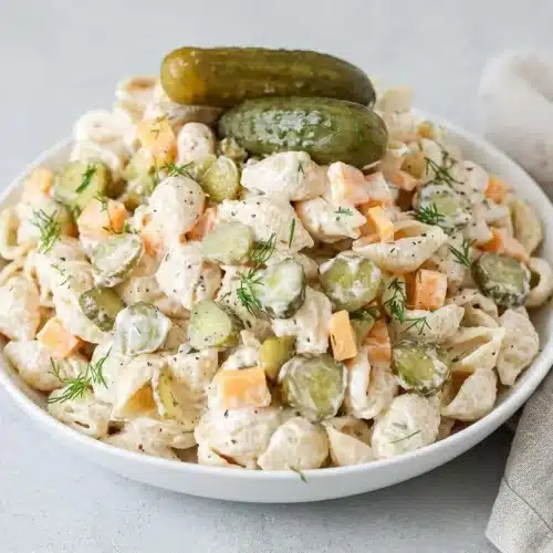 Creamy dill pickle pasta salad with glossy shell pasta, crisp pickle slices, cheddar cubes, and fresh dill.