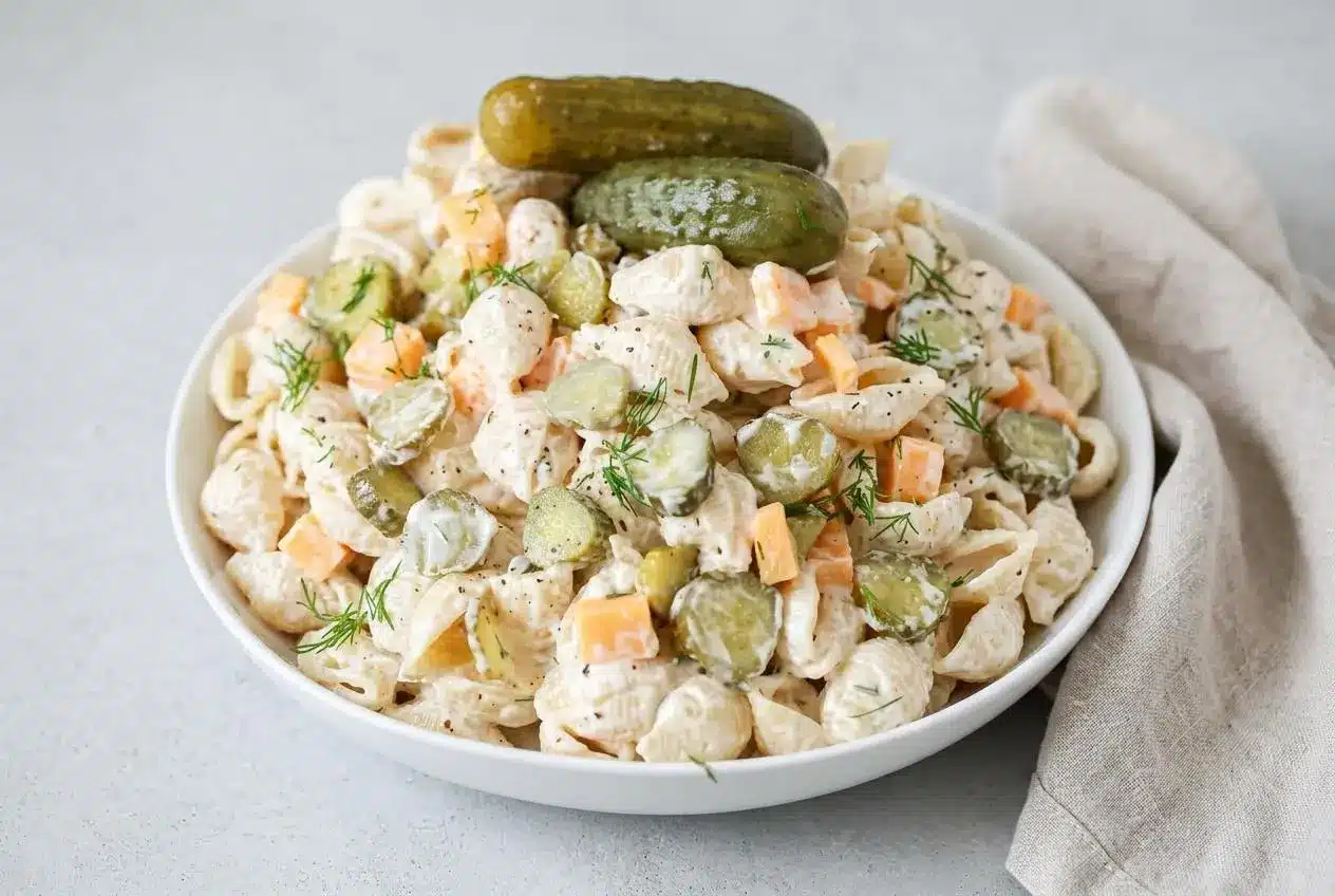 Creamy dill pickle pasta salad with glossy shell pasta, crisp pickle slices, cheddar cubes, and fresh dill.