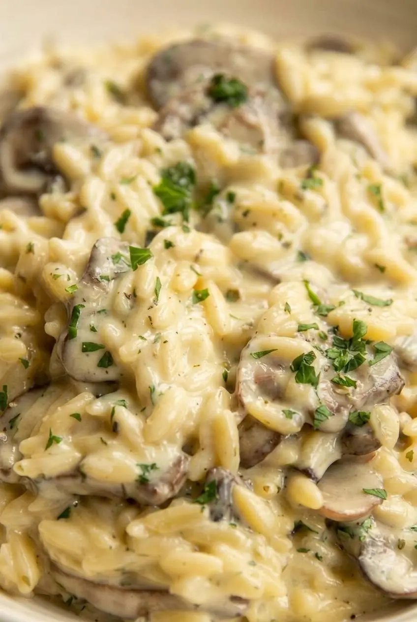 Close-up of glossy orzo pasta coated in creamy garlic sauce with browned mushrooms and fresh thyme.