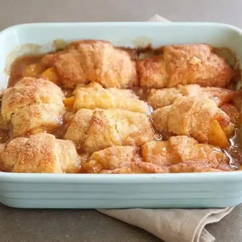 Golden baked crescent roll peach dumplings bubbling in sweet cinnamon butter syrup.