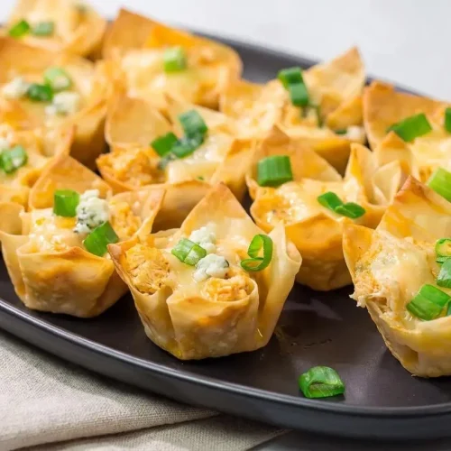 Baked buffalo chicken wonton cups with golden crispy corners, creamy cheese filling, and chopped green onions.