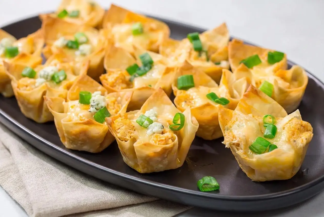 Baked buffalo chicken wonton cups with golden crispy corners, creamy cheese filling, and chopped green onions.