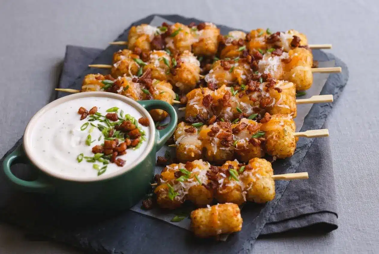 Crispy loaded tater tot skewers topped with melted cheese, chopped bacon, and green onions on a platter with ranch dip