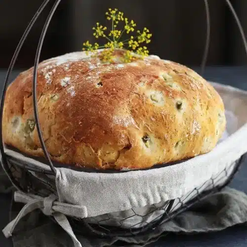 Freshly baked dill pickle bread with a golden crust and tender crumb flecked with dried dill and diced pickles