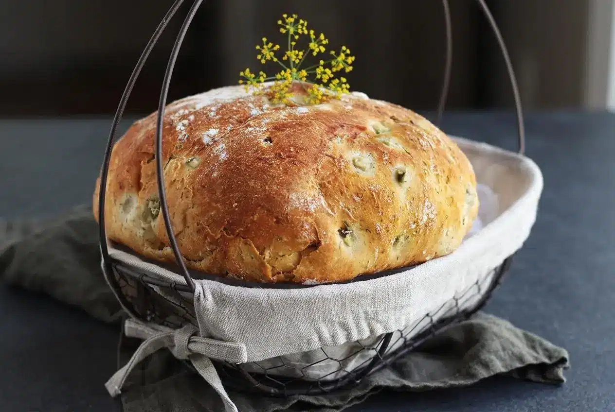 Freshly baked dill pickle bread with a golden crust and tender crumb flecked with dried dill and diced pickles