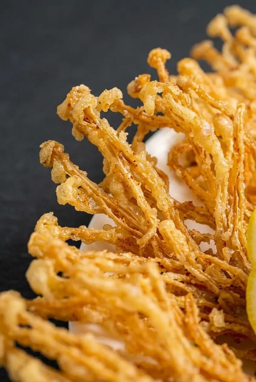 Close-up of fried enoki mushroom fan showing lace-like batter bubbles and brittle golden edges.