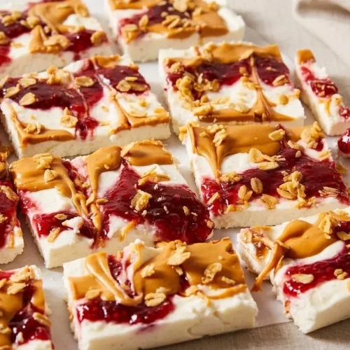 Frozen cottage cheese bark topped with creamy peanut butter swirl, raspberry jam, and crunchy granola.