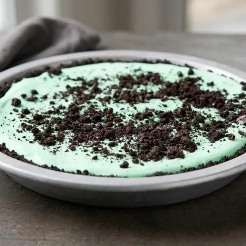 Finished grasshopper pie recipe with creamy pastel-green mint mousse in a dark Oreo cookie crust.