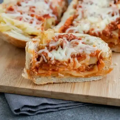 Baked lasagna stuffed garlic bread in hollowed French loaf boats with golden crust, beef sauce, noodles, and melted cheese.