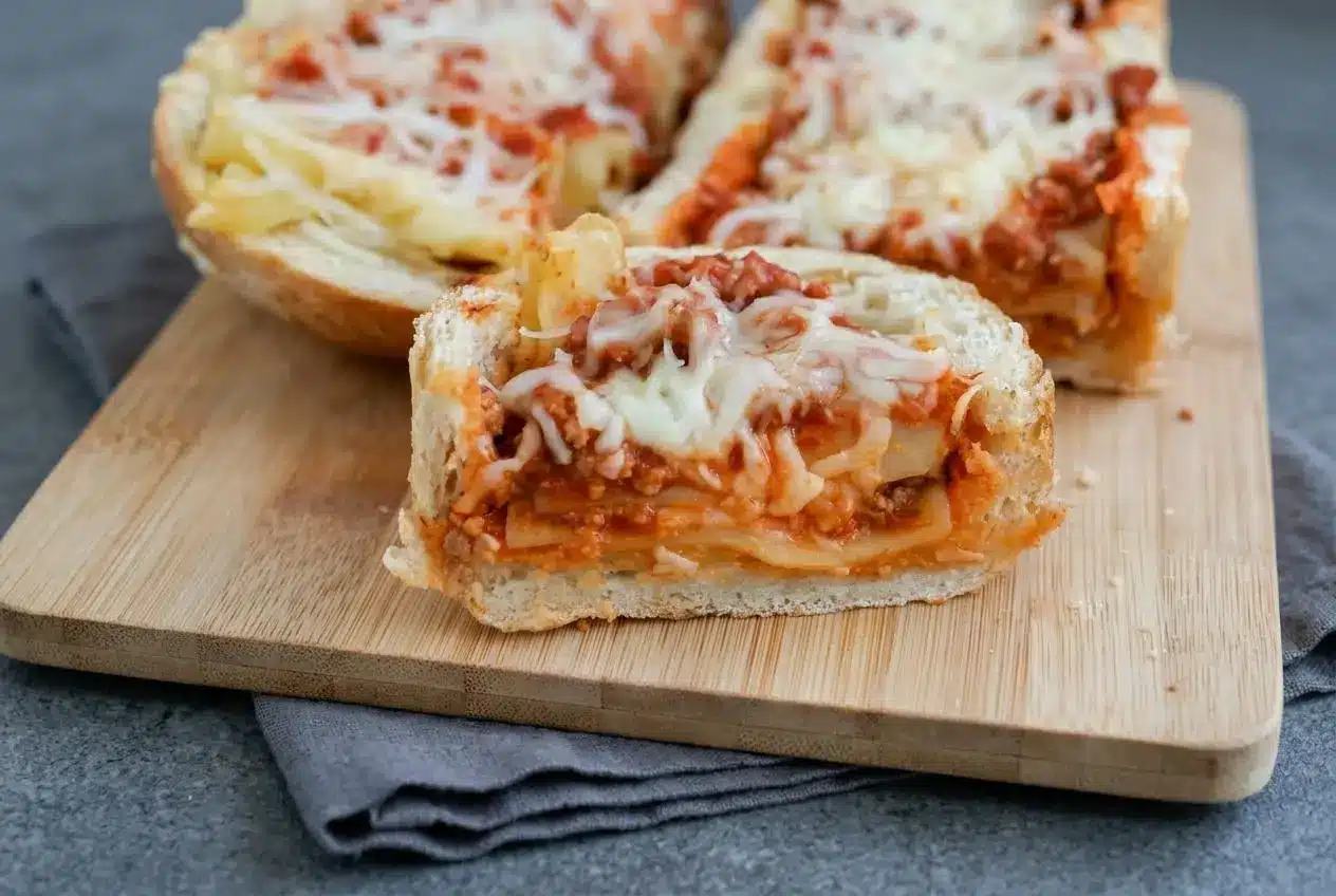 Baked lasagna stuffed garlic bread in hollowed French loaf boats with golden crust, beef sauce, noodles, and melted cheese.