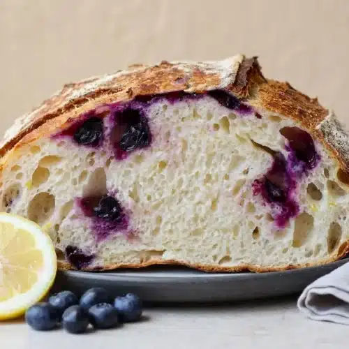 Round artisan lemon blueberry sourdough bread with a deeply golden blistered crust and burst berries