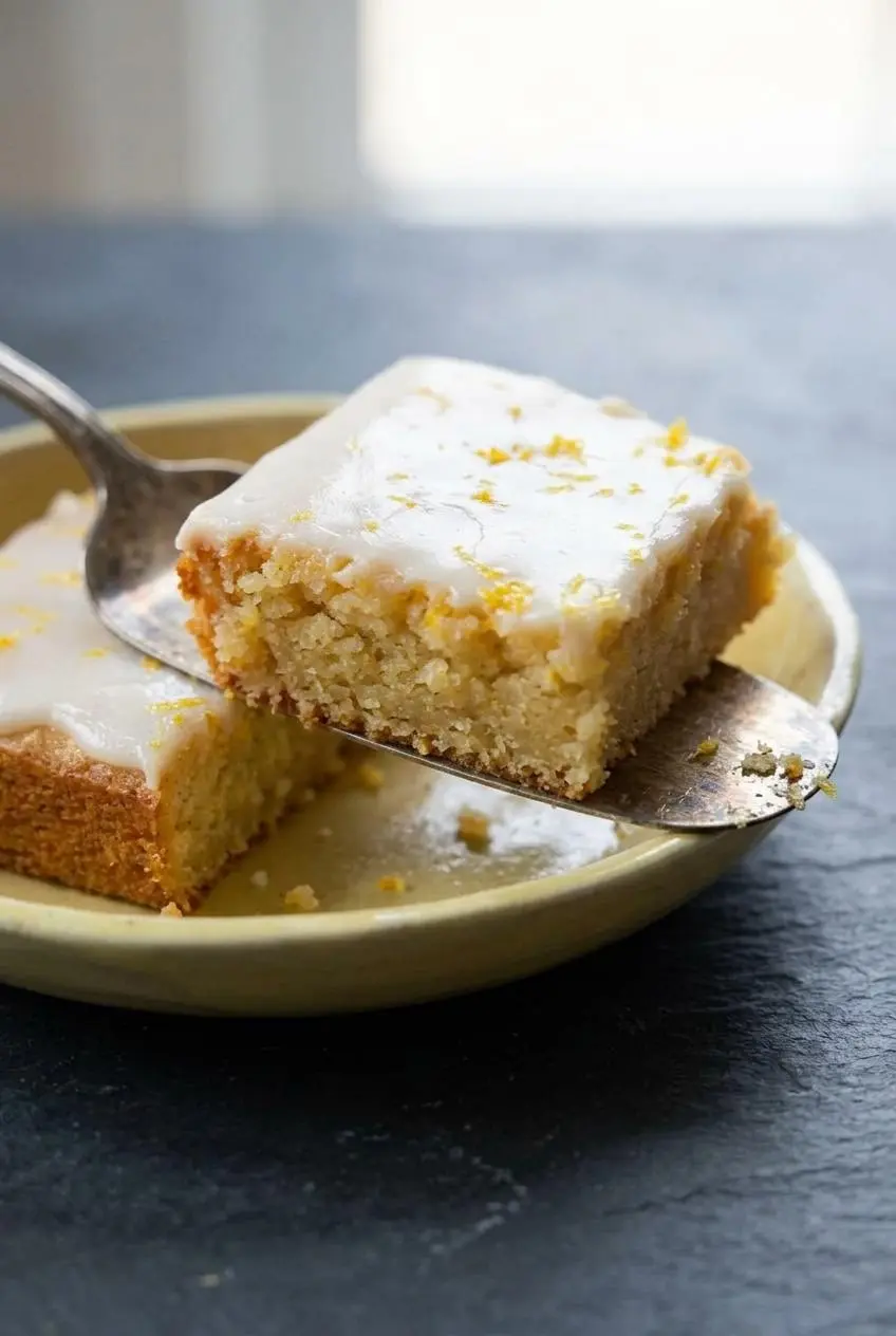 Close-up of a lifted lemon brownie square showing the dense single-layer crumb, golden edge, and thick white chocolate glaze.