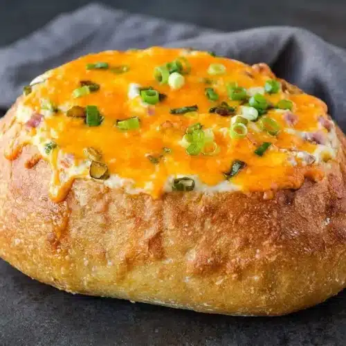 Warm mississippi sin dip baked in a round French bread bowl with bubbling cheddar, cubed ham, and sliced green onions.