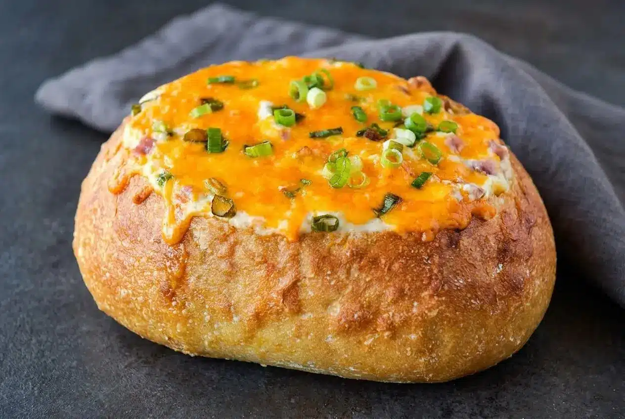 Warm mississippi sin dip baked in a round French bread bowl with bubbling cheddar, cubed ham, and sliced green onions.