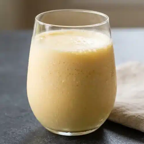 Chilled glass of homemade orange julius recipe with pale pastel orange slush and a thick white frothy top.