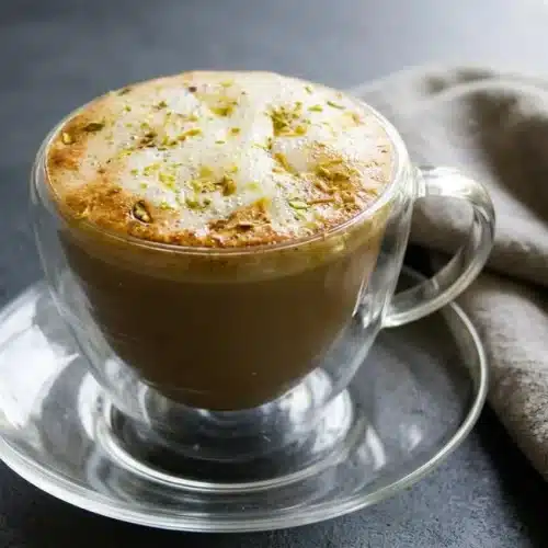 Hot pistachio latte recipe in a mug with velvety pale-green foam and thinly sliced green pistachios on top