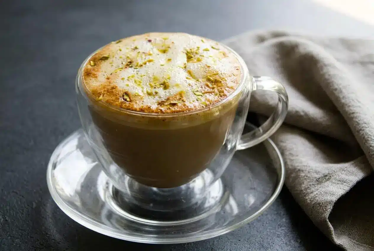 Hot pistachio latte recipe in a mug with velvety pale-green foam and thinly sliced green pistachios on top