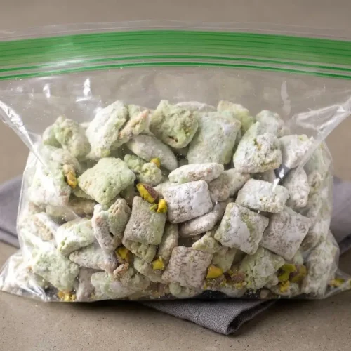 Pistachio puppy chow cereal clusters coated in powdered sugar with a pale pastel green glaze
