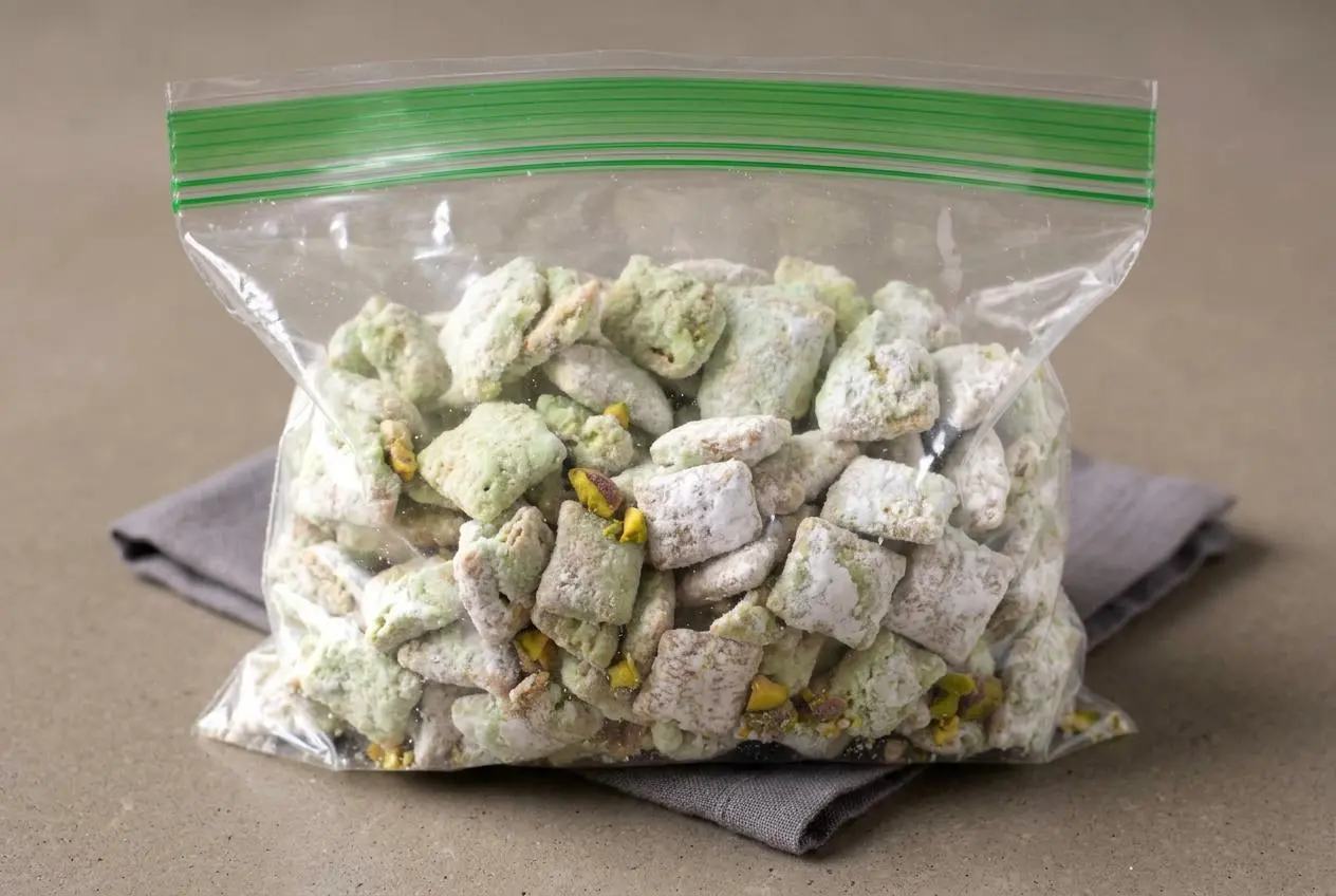 Pistachio puppy chow cereal clusters coated in powdered sugar with a pale pastel green glaze