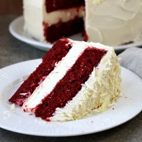 Tall red velvet cheesecake cake with moist red cake layers, a creamy baked cheesecake center, and tangy white frosting.