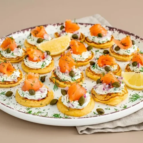 Smoked Salmon Blini with golden mini pancakes topped with cool herbed crème fraîche, salmon ribbons, and fresh dill.