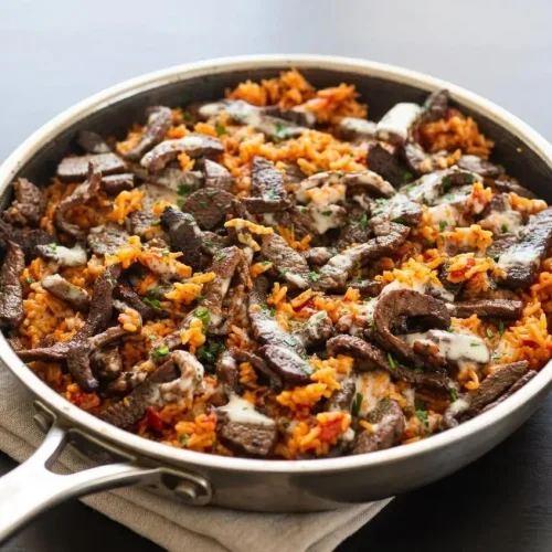 Skillet of steak and queso rice with browned sirloin strips, fluffy tomato basmati rice, velvety white queso, and cilantro