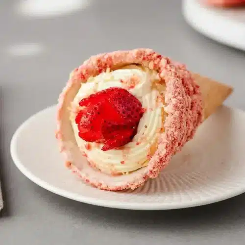 Strawberry crunch cheesecake cones filled with creamy vanilla cheesecake and topped with fresh strawberry roses.