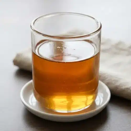 Glass bottle of golden-amber Sugar Cookie Latte Syrup with a clear, glossy finish on a kitchen surface