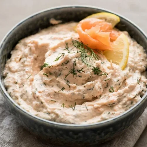 Bowl of velvety smoked salmon dip topped with fresh dill and lemon slices.